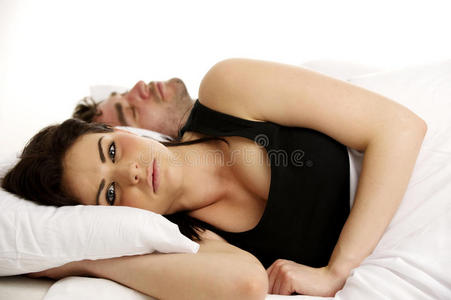 一个女人躺在一个熟睡的男人旁边的白床上