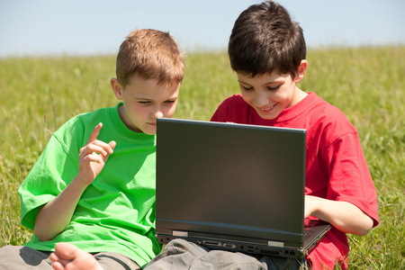 两个男孩与笔记本电脑在草地上