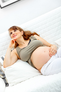 美丽的孕妇坐在沙发上并按住她的肚子里的梦