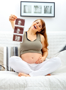 笑美丽怀孕女性坐在沙发，回声在手