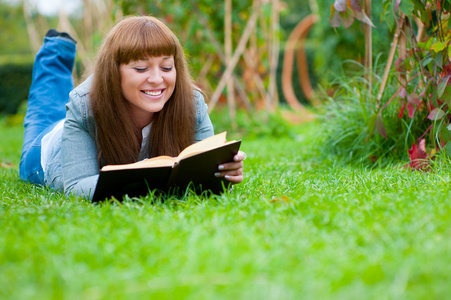 读一本书躺在草地上的年轻女子