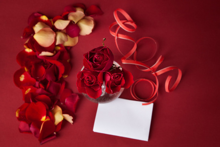 束红玫瑰与白卡和玫瑰花瓣红色背景上