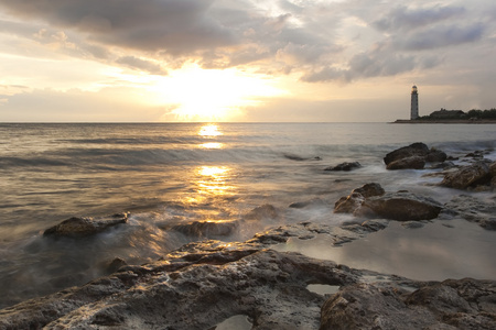 美丽的岩石海海滩与灯塔的日落