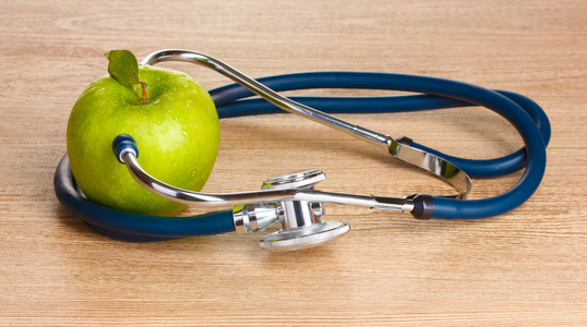 医用听诊器和木制背景上的绿色苹果