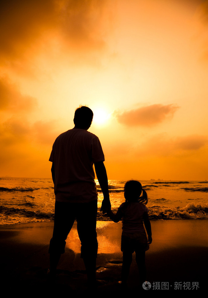 父亲牵着小女孩的手在海滩上的剪影
