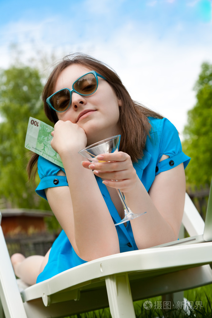女人躺在休息室和持有一个玻璃酒杯与 banknot