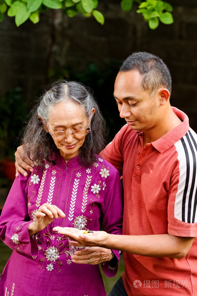 亚洲年轻男人的拥抱和帮助年迈的母亲吃药