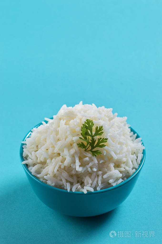 煮熟的纯白色印度香米与香菜在蓝色背景上的蓝色碗米饭