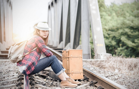 时髦的年轻女孩与背包坐在铁路上