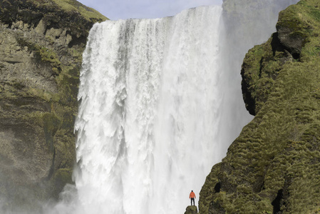 穿红色上衣的年轻男子站在背后，冰岛斯科加瀑布瀑布悬崖上跳下