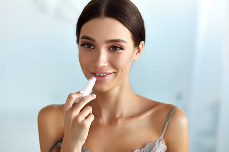 美脸的美丽女人适用润唇膏在嘴唇上。皮肤护理