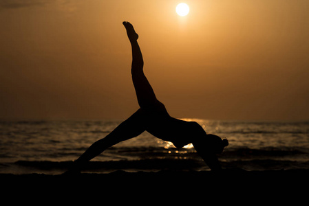 在日落时练瑜伽在海边的女孩
