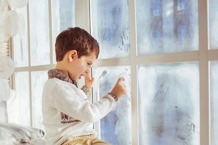 在冬天冻结窗口上绘制肖像的小男孩