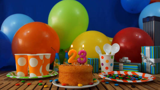 生日蛋糕上仿古的木桌上的五颜六色的气球 礼品 塑料杯和塑料板与糖果和蓝色背景墙里的背景