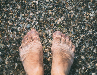 人的脚在清澈的水的海卵石