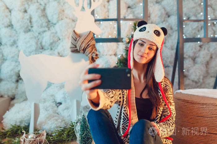 美丽的年轻女子，在滑稽的帽子，坐在圣诞装饰品和使自拍照的背景