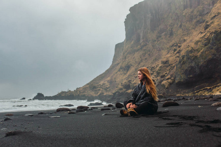 女人坐在海边与黑色的沙子