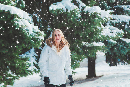 年轻开朗的女人在户外玩得开心。在最冷的冬天背景下的树和雪。女孩穿着一件白色外套和黑色手套