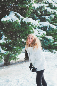 年轻开朗的女人在户外玩得开心。在最冷的冬天背景下的树和雪。女孩穿着一件白色外套和黑色手套