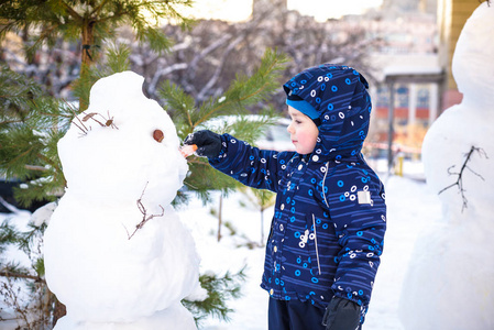 搞笑小小孩男孩做雪人和吃胡萝卜，玩玩雪，在户外对寒冷的一天。积极的休闲儿童冬季