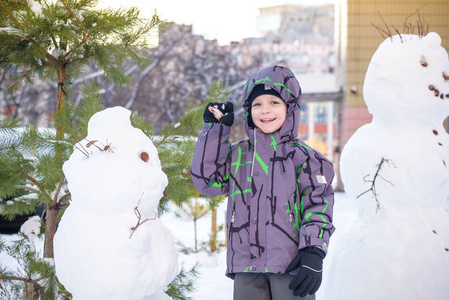 搞笑小小孩男孩做雪人和吃胡萝卜，玩玩雪，在户外对寒冷的一天。积极的休闲儿童冬季