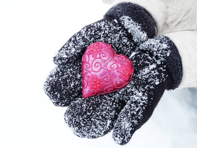 女人的手在手套与红色的心，在雪上