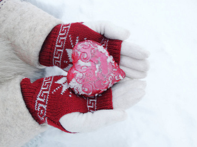 女人的手在手套与红色的心，在雪上