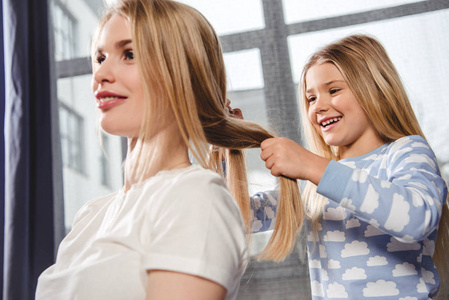 妈妈给小女儿编辫子母亲用梳子梳孩子们的头发女儿美丽发型的概念