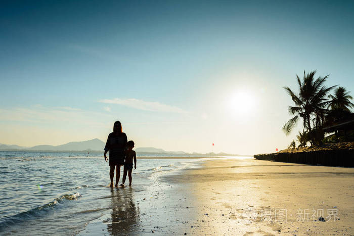 母亲和儿子在日出期间在美丽的海滩上行走