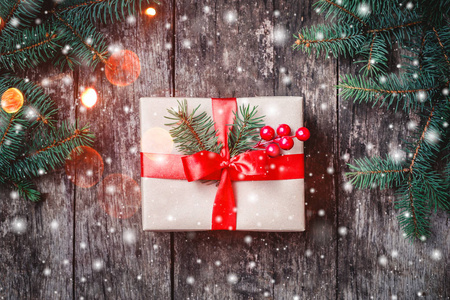 圣诞礼品盒红丝带，冷杉的枝条，雪花飘落在木制的背景。圣诞节和新年快乐组成。平躺，顶视图