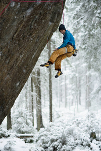 极端的冬季运动攀登。年轻的男性攀岩岩壁。白雪皑皑的丛林的背景
