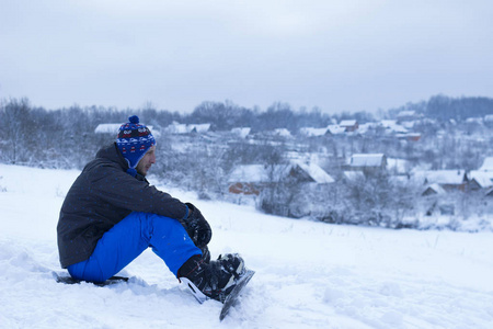 年轻人坐在雪地上扣在滑雪板图片