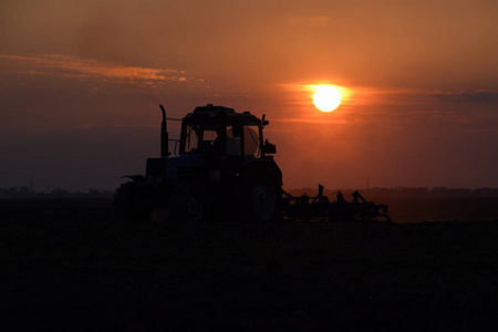 拖拉机在夕阳下犁地.日落背景上的拖拉机剪影。