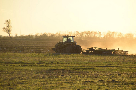 日落时的拖拉机犁地。 收获后秋季耕作土壤。 赛季结束了。