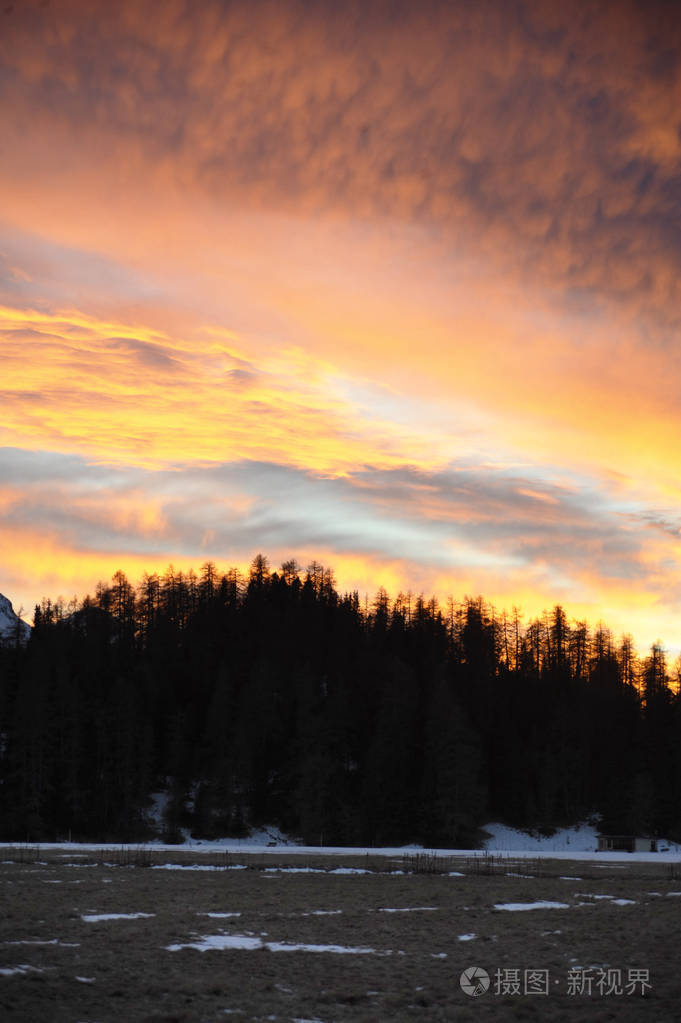 美丽的冬天日落橙云天空和雪的阿尔卑斯山和恩加丁地区森林