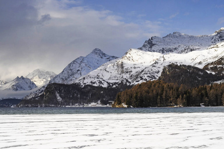 恩加丁谷在瑞士锡尔斯玛丽亚村庄与阿尔卑斯山和结冰的湖面上的雪