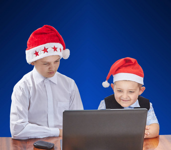 在帽圣诞老人的蓝色背景孩子看着一台笔记本电脑