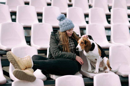 年轻的时髦女孩与她的宠物爱沙尼亚猎犬狗玩，俊平和拥抱和室外在玩老体育场