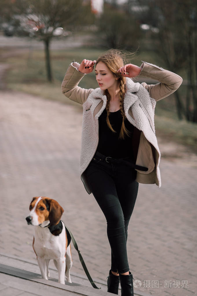 年轻的时髦女孩与她的宠物爱沙尼亚猎犬狗玩,开心户外公园里照片-正版