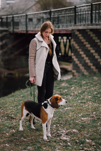 年轻的时髦女孩与她的宠物爱沙尼亚猎犬狗玩，开心户外公园里