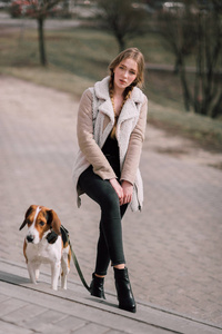 年轻的时髦女孩与她的宠物爱沙尼亚猎犬狗玩，开心户外公园里