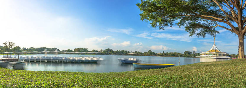 在平静的湖面，一条船在前景和蒜銮拉玛九公共公园曼谷 Ratchamangkala Pavilion 在下午的背景