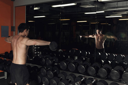 年轻英俊的男人，训练自己的肩膀上哑铃健身房在镜子