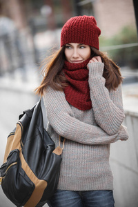 年轻漂亮的女孩在一个温暖的毛衣，一顶红色的帽子和围巾和在他肩上的背包的肖像