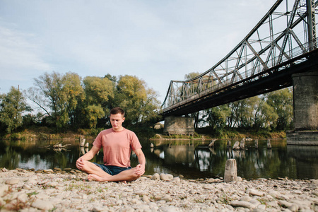 男人练瑜伽老桥附近的河岸上