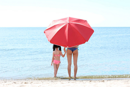 母亲和女儿带着雨伞在海滩上放松