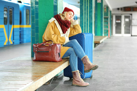 女人拿着手提箱在火车站等着