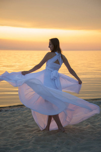 美丽的女孩在一个长的白色礼服走在海边