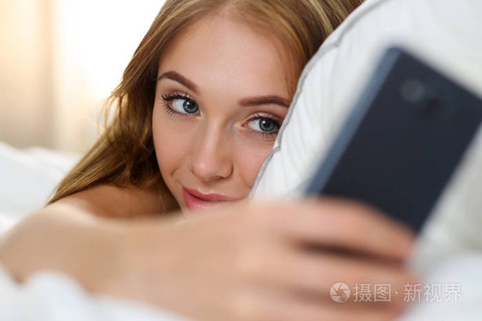 年轻漂亮的金发女人躺在床上抱着手机