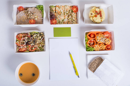 健康营养计划。新鲜的日常饭食交货。一 蔬菜 肉类和水果在铝箔盒 制卡 笔记本和铅笔在白色背景上的餐厅，食物